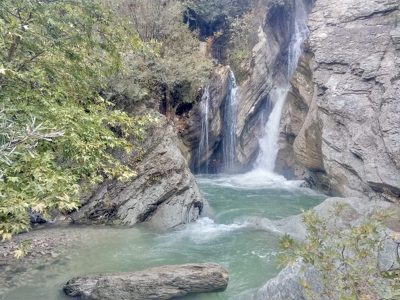 Bogovë Waterfall falling into a green pool between rocks.