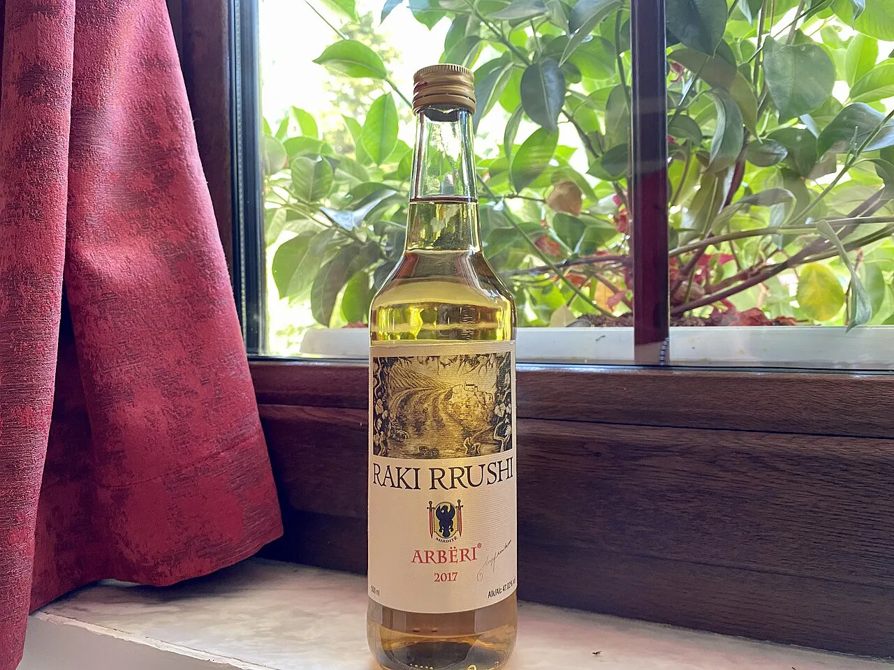 A bottle of grape raki on a window sill.