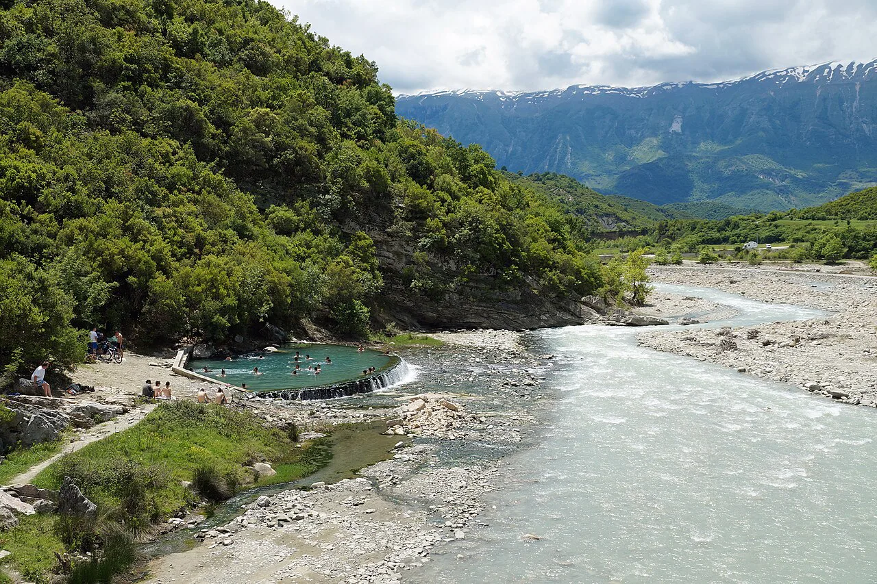 Thermal pools beside the Lengarica river at Bënjë, with snow-capped mountains behind.
