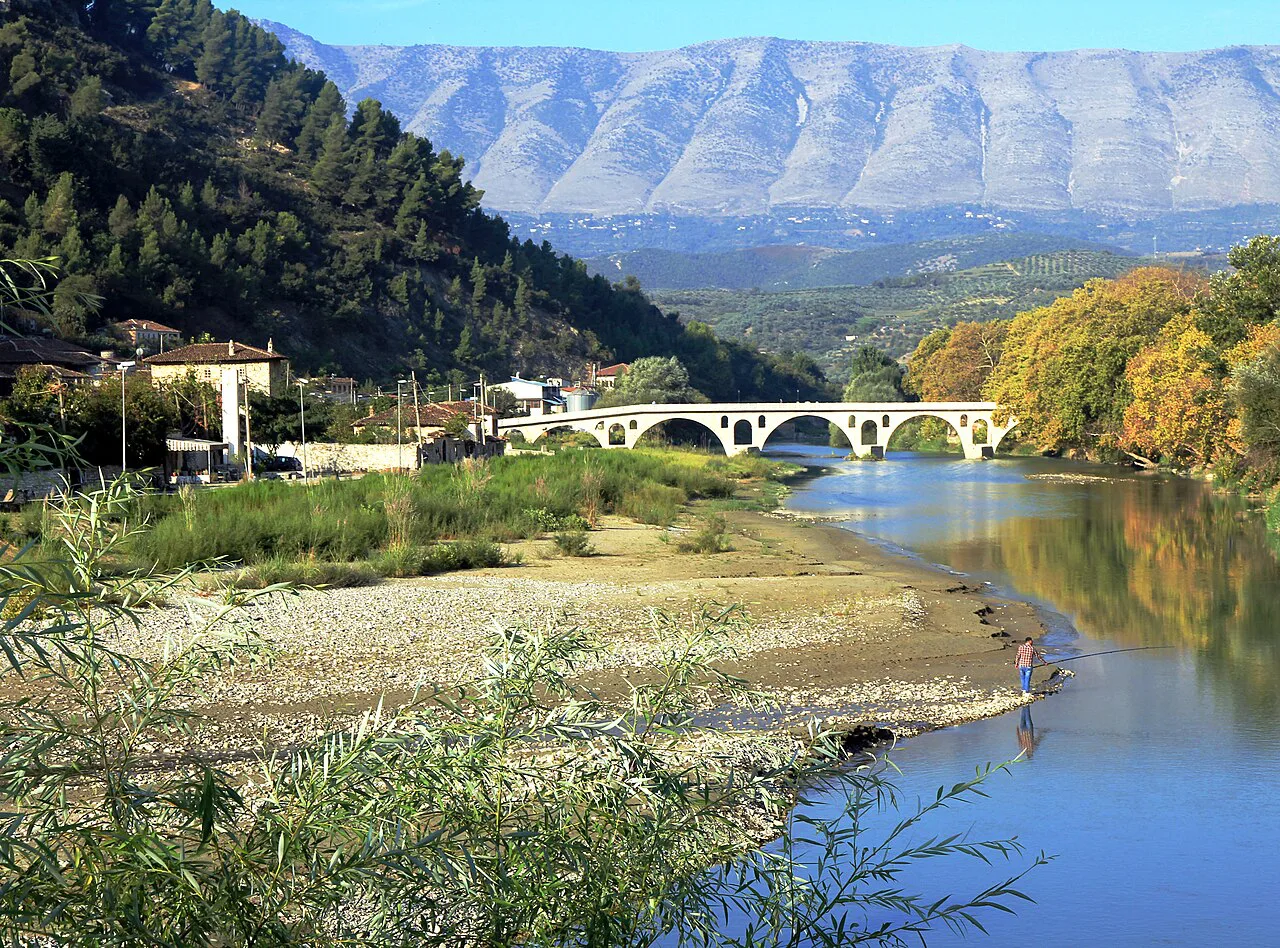 The Gorica Bridge over the Osum river in Berat, with mountains beyond.