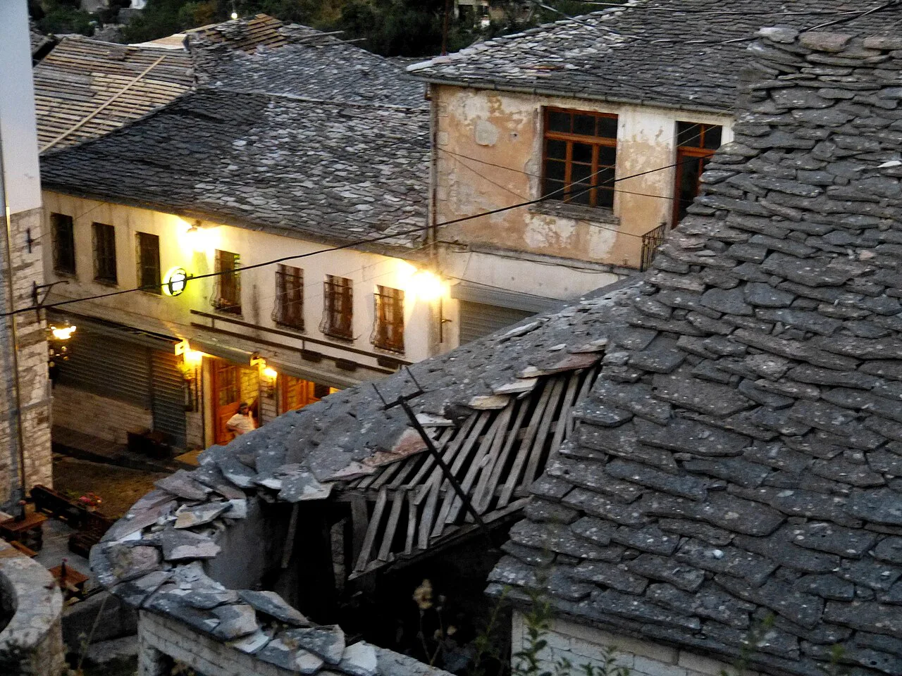 Lit restaurants beneath stone roofs in Gjirokastër's old town in the evening.