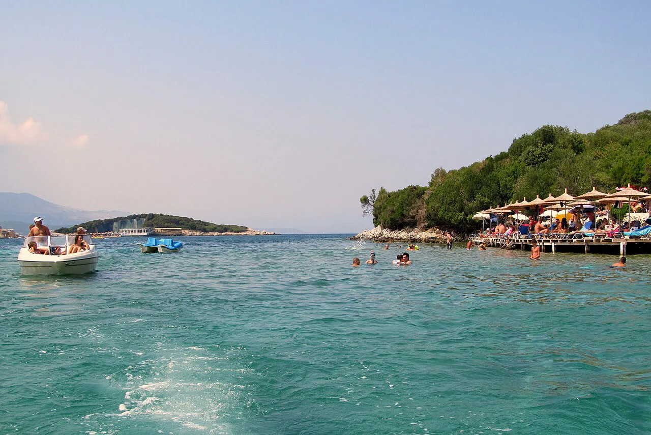 Swimmers and beach umbrellas at Ksamil beside a wooded islet.