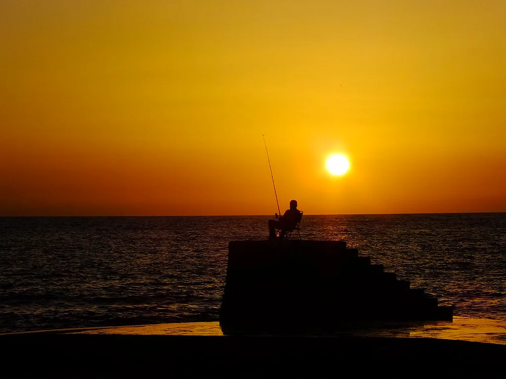 A fisherman silhouetted against the sunset on the coast at Dhërmi.