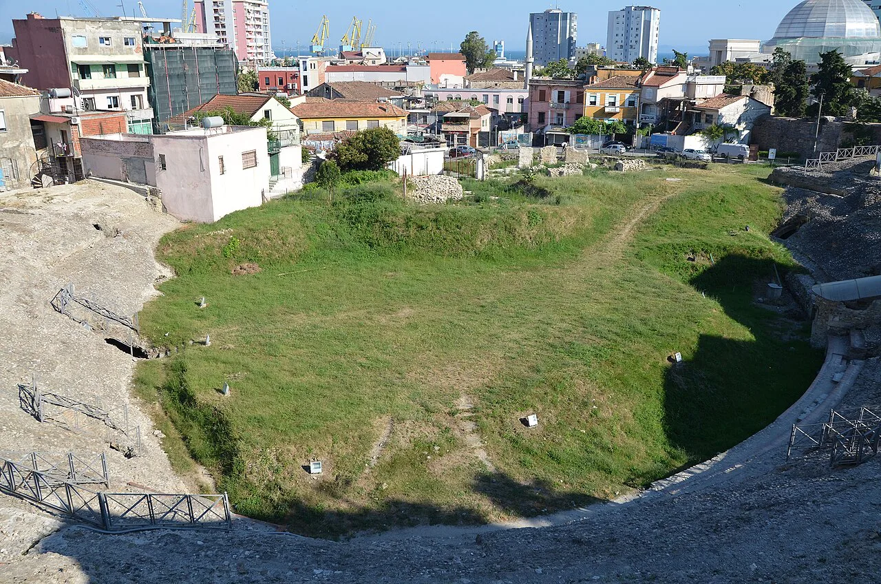 The grassy arena of the Roman amphitheatre in Durrës, surrounded by the city.
