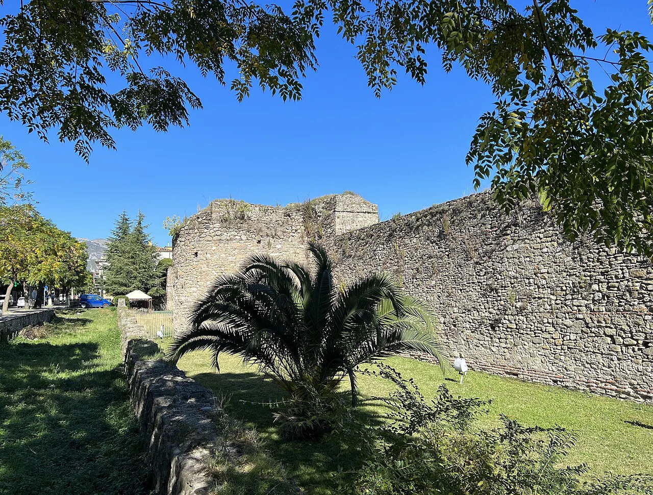 The stone walls of Elbasan Castle framed by palms and trees.