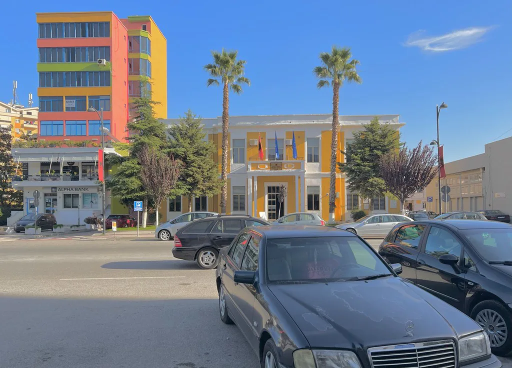 Brightly painted buildings and palm trees on a street in Fier.