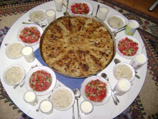 A large tray of flija served with bowls of salad and yoghurt.