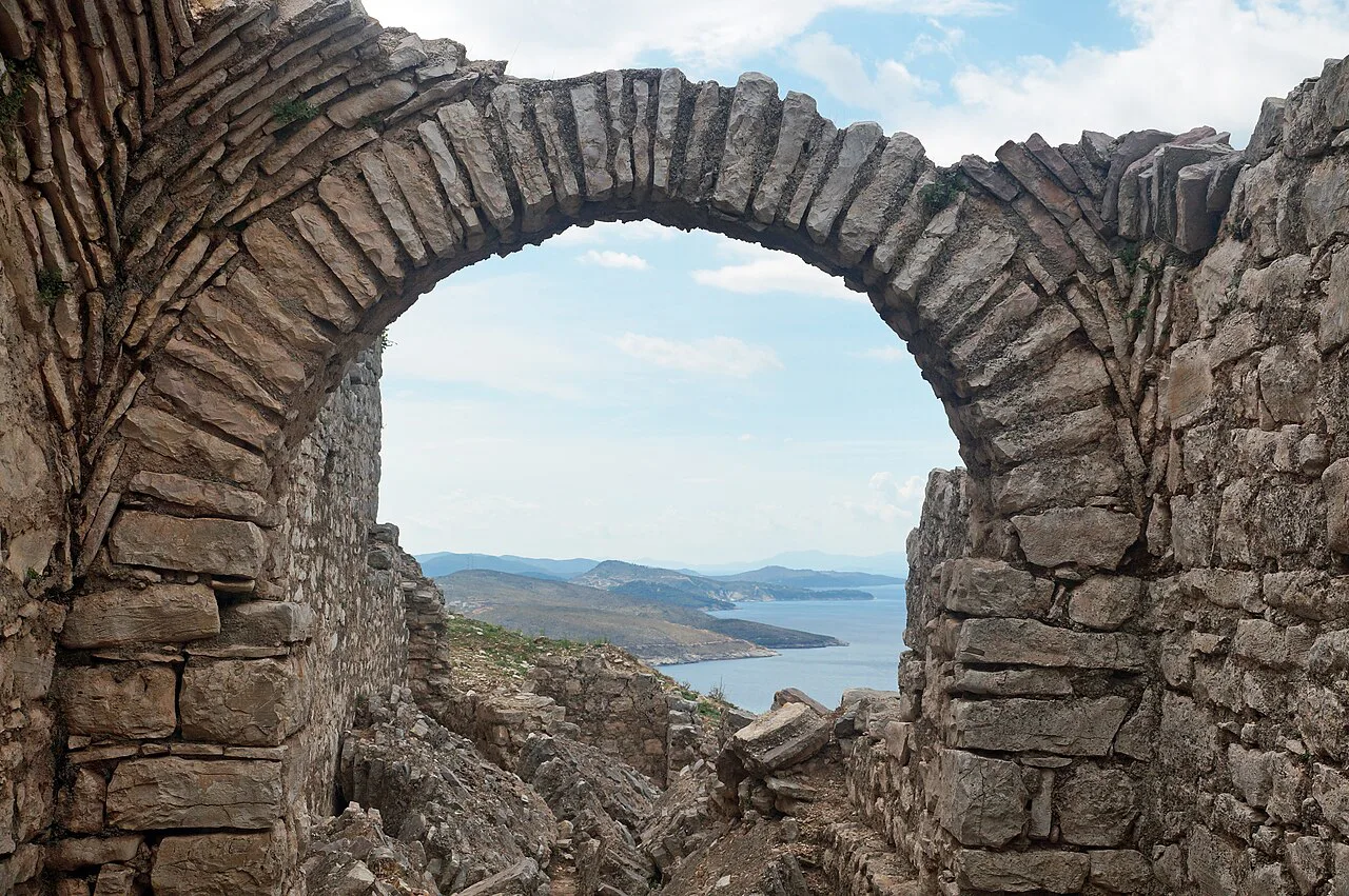 A ruined stone arch at the Forty Saints Monastery above Sarandë, framing a view of the coast.