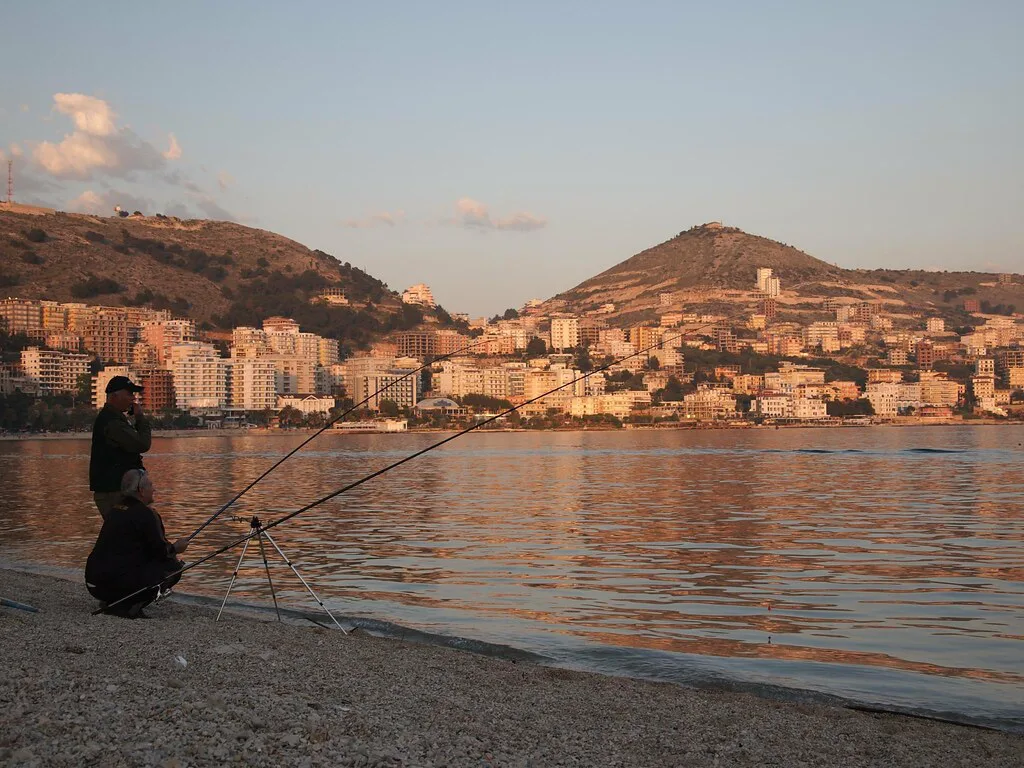 Sarandë's seafront and hillside buildings across the bay at sunset.