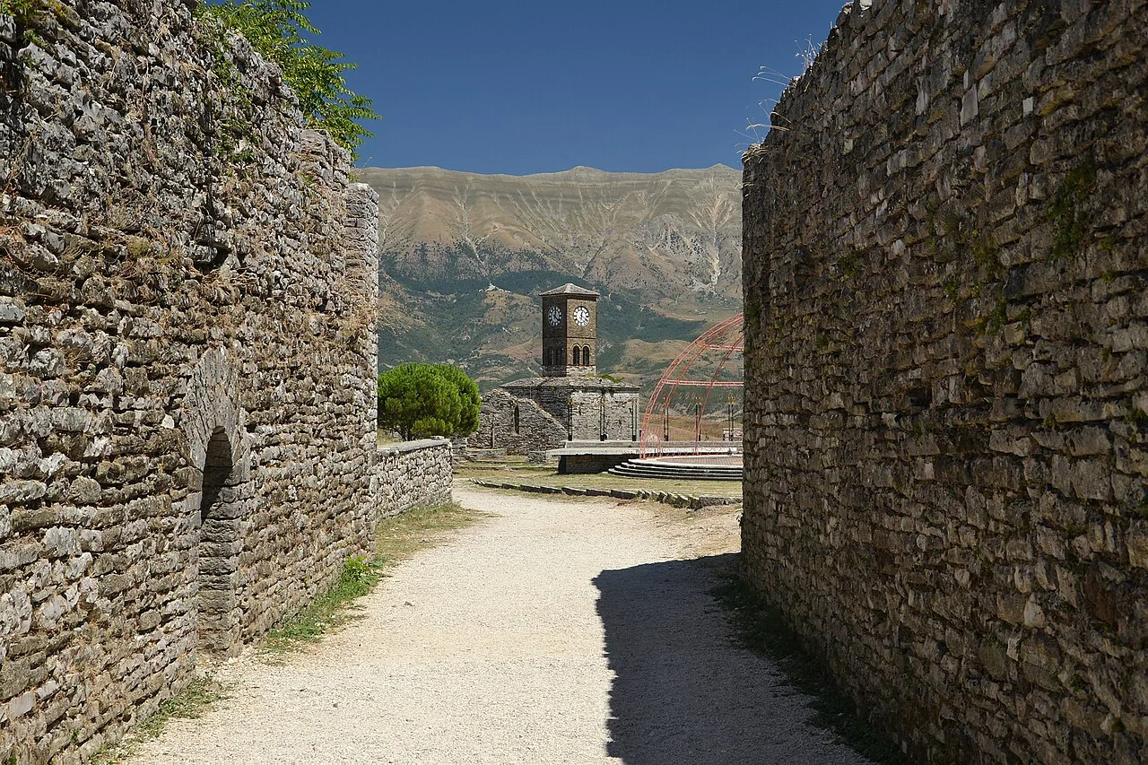 A path between the stone walls of Gjirokastër Castle, with the clock tower ahead.