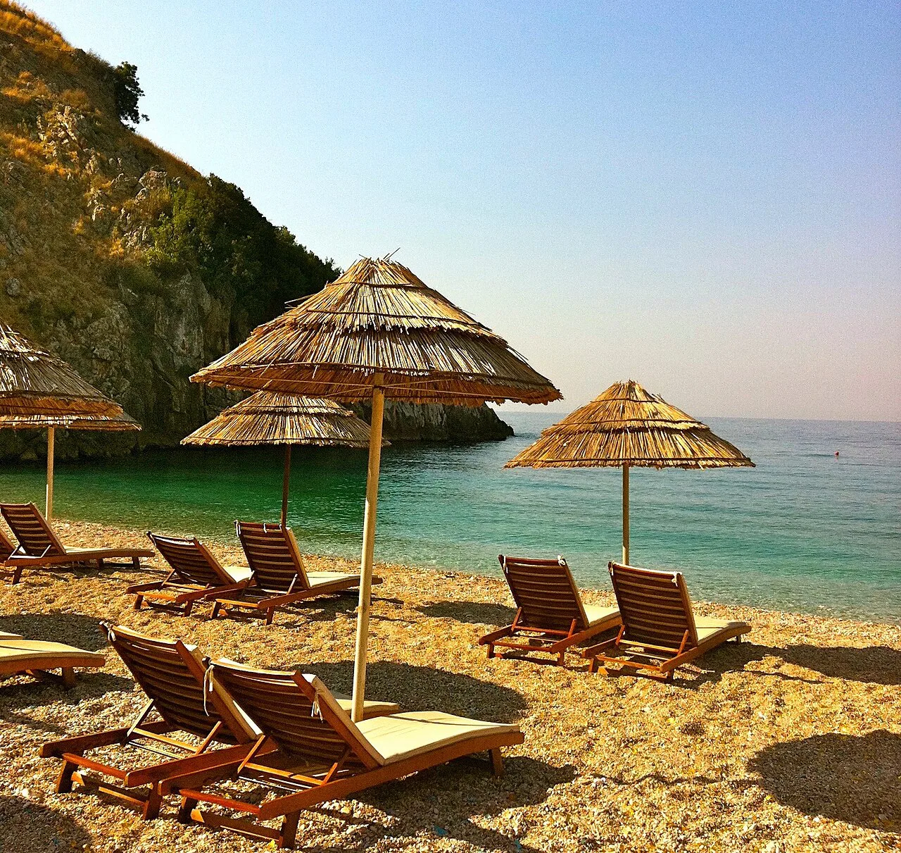 Straw parasols and sun loungers on a beach in Himarë.