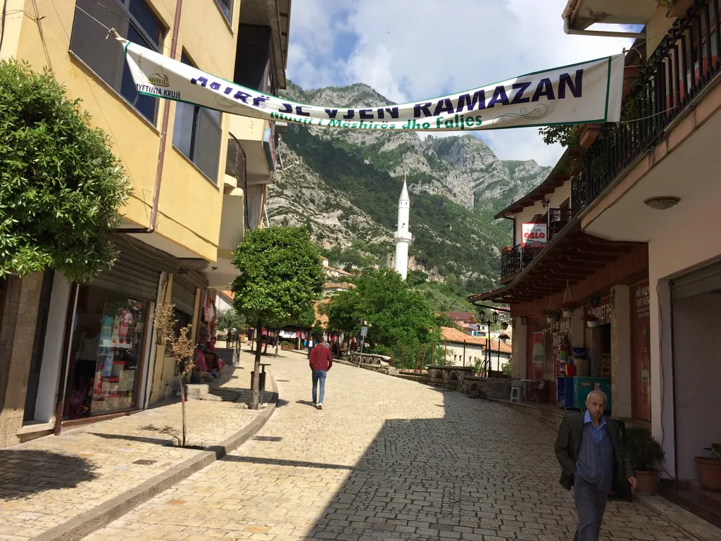 A cobbled shopping street in Krujë with a minaret beyond.