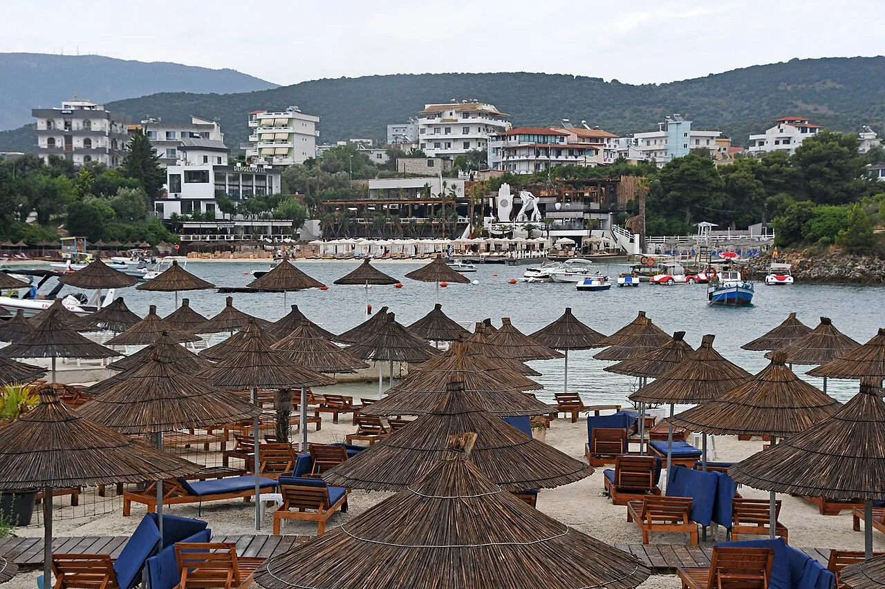 Rows of straw parasols on the beach at Ksamil with the village behind.