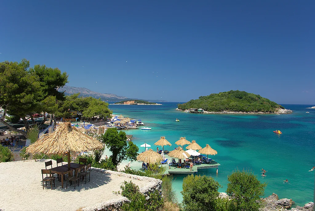 A beach bar with straw parasols above the turquoise water and islets at Ksamil.