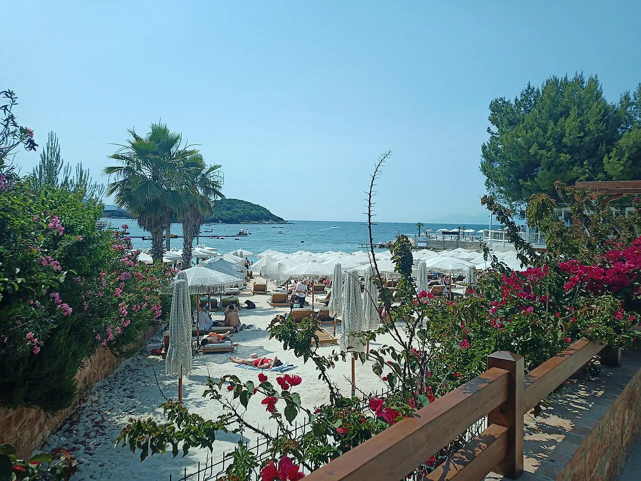 A beach in Ksamil framed by palms and flowering shrubs.