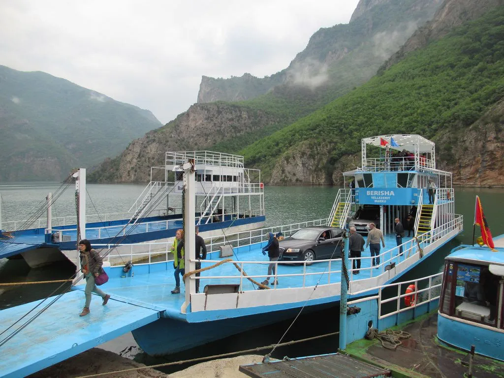 Ferries moored at the jetty on Lake Koman beneath steep wooded mountains.