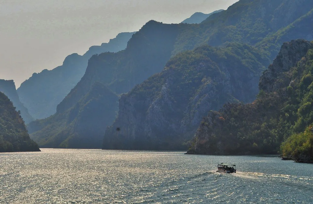 A boat travelling along the narrow, mountain-lined reservoir of Lake Koman.