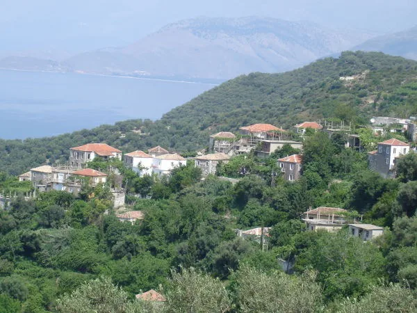 Stone houses of Lukovë village on a green hillside above the Ionian Sea.