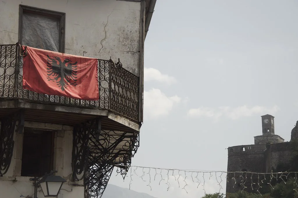 An Albanian flag on a balcony with Gjirokastër Castle in the background.