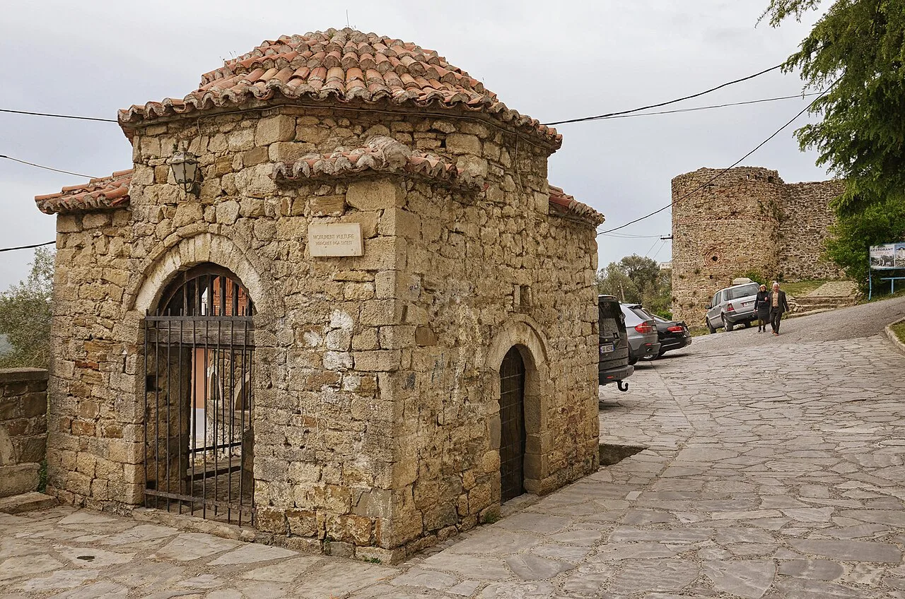 The domed former Bektashi well beside the road in Prezë, with the castle wall behind.