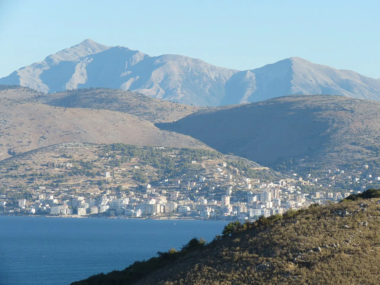 Sarandë spread along its bay beneath the mountains, seen from Manastir.