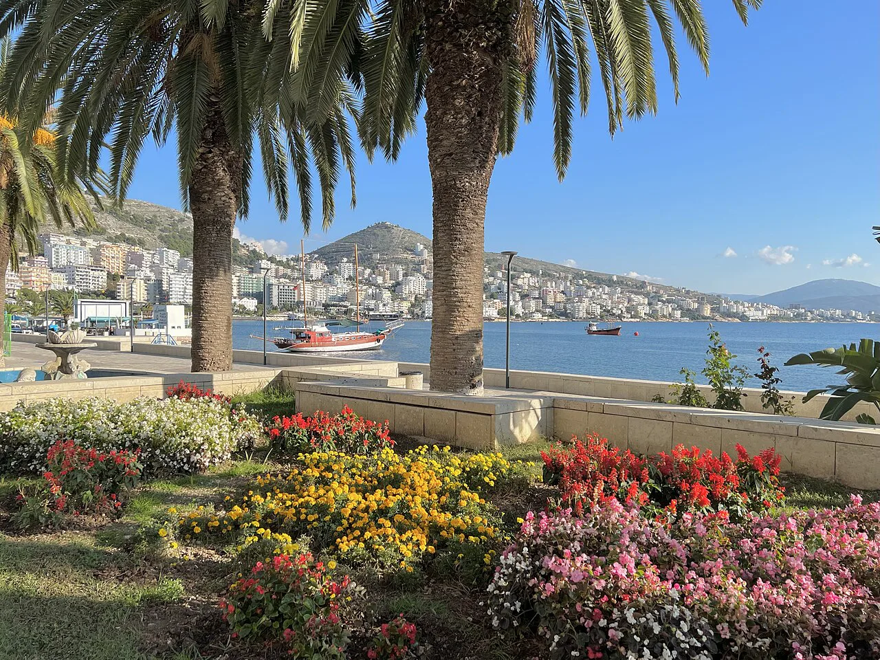 Flower beds and palm trees on the Sarandë promenade, overlooking the bay.