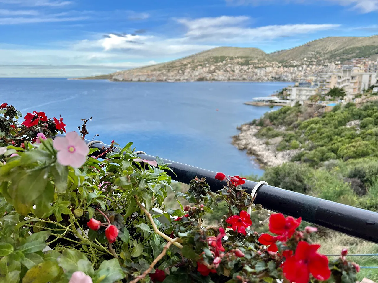 A balcony view over Sarandë Bay framed by red flowers.