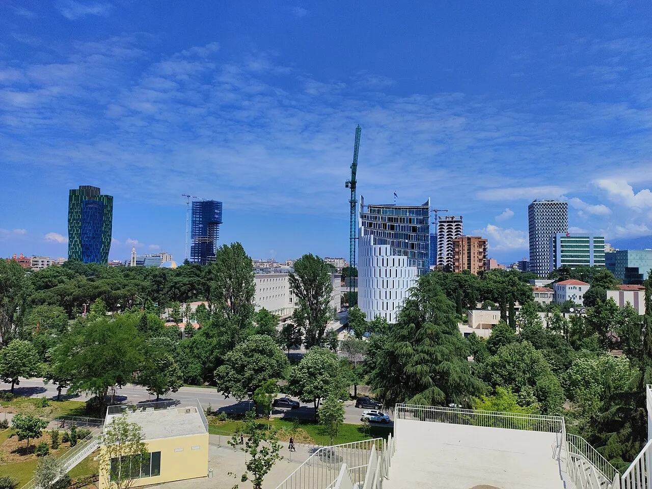 Modern towers on the Tirana skyline seen across a park.