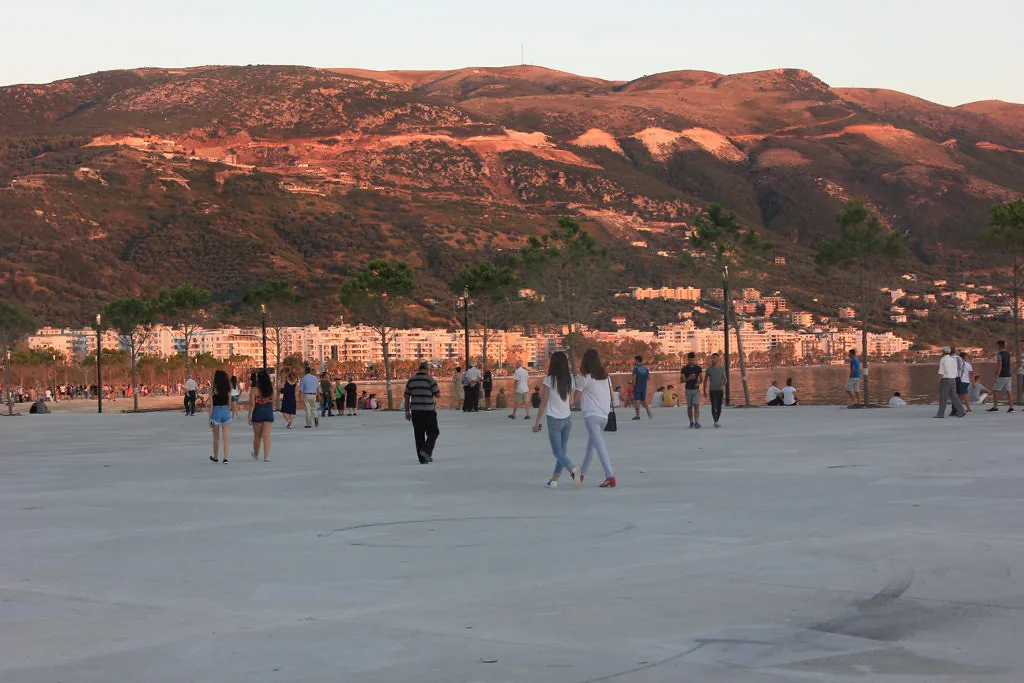 People strolling on the waterfront promenade in Vlorë with mountains behind.