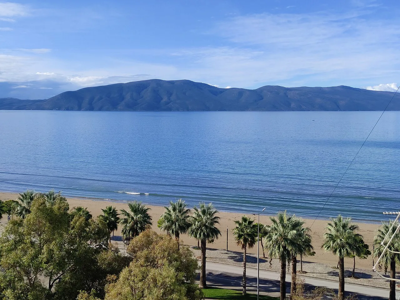 Palm-lined beach in Vlorë with the bay and mountains beyond.
